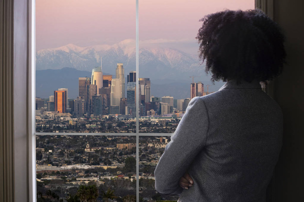 Чорний жіночий бізнес жінка дивиться вікно офісу в Лос-Анджелесі. Вона виглядає як жіночий архітектор мислення міського розвитку або міського голови або губернатора планування зонування закони.  - Фото, зображення
