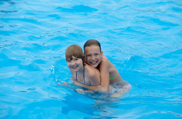 Τα ευτυχισμένα κοριτσάκια διασκεδάζουν κολυμπώντας στην πισίνα. Υπέροχη διάθεση. - Φωτογραφία, εικόνα