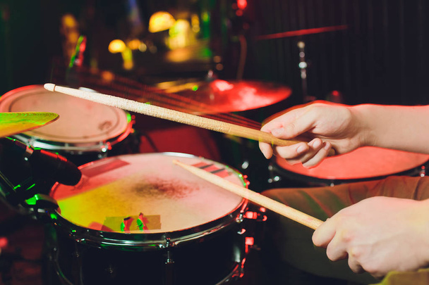 the man plays the drums, the game is on the working drum with sticks close-up. On the background of colored lights with splashes of water. Musical concept with a working drum. - Foto, imagen