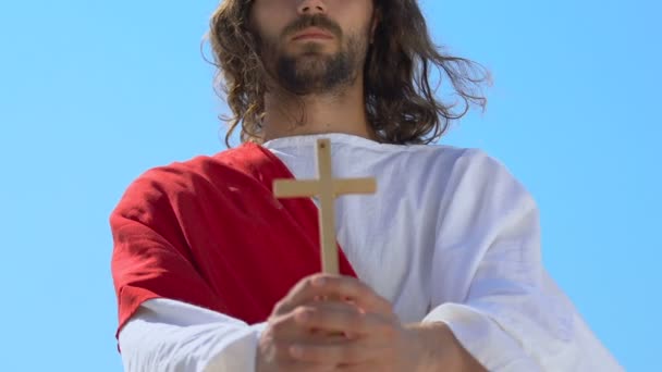 Jezus in gewaad toont houten kruis bij camera, christelijke religie symbool, close-up - Video