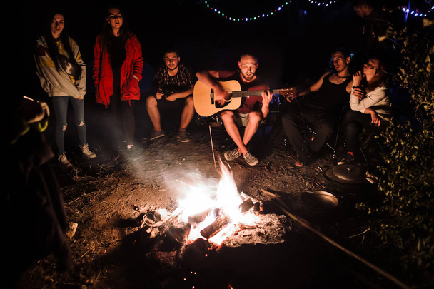 Amigos viajantes refrigerando na fogueira grande, cantando canções e pla
 - Foto, Imagem