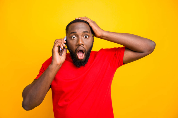 Photo of feared trembling black man with his hand holding head hearing some bad news while talking by phone while isolated with yellow background - Фото, зображення