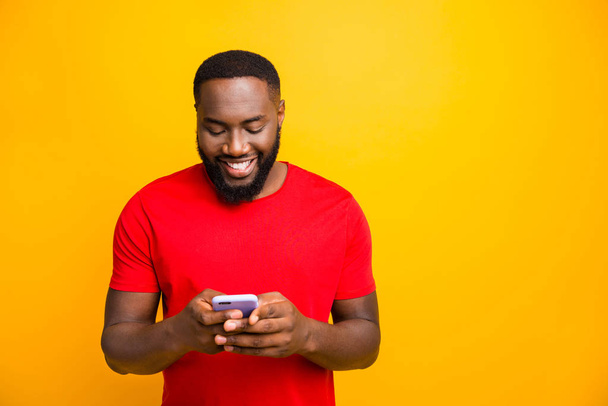 Photo of glad cheerful nice cute black man browsing through his phone and chatting to his friend while isolated with yellow background - Fotografie, Obrázek