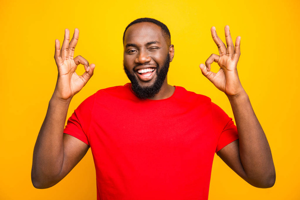 Photo of cheerful funny black man blinking you giving hint that everything is perfect while isolated with yellow background - Fotografie, Obrázek