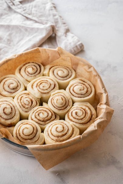 Raw cinnamon rolls in baking plate on kitchen table. Copy space. - Фото, изображение