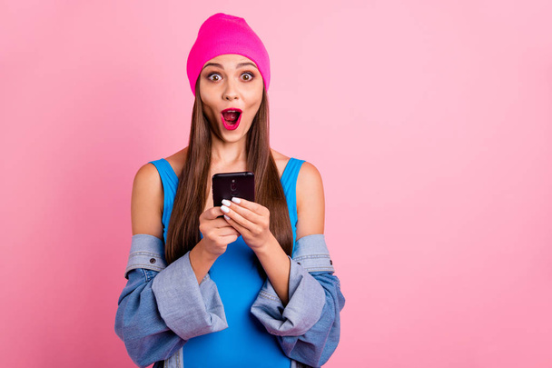 Portrait of impressed millennial holding device screaming wow omg wearing blue bodysuit isolated over pink background - Foto, imagen