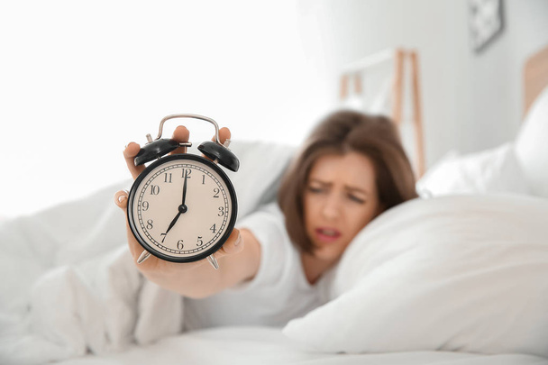 Morning of displeased sleepy young woman with alarm clock in bedroom - Fotó, kép