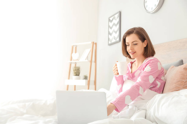 ベッドでコーヒーを飲むラップトップを持つ美しい若い女性の朝 - 写真・画像