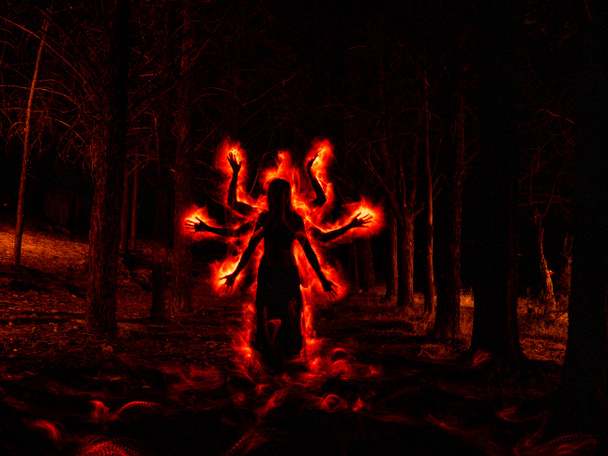 Image of woman in the dark forest silhouetted with red fire effect on the sides - Photo, Image