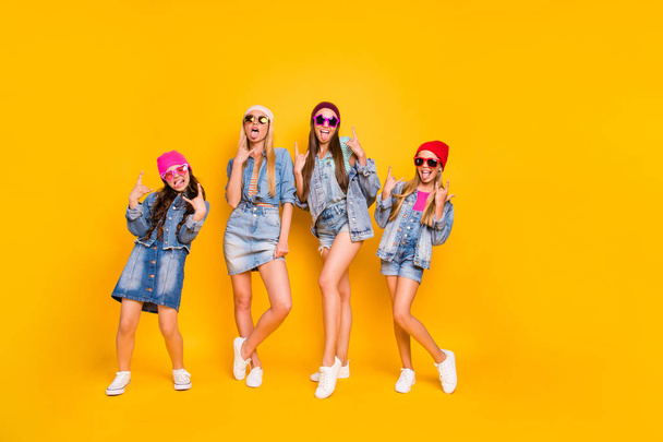 Full length body photo of group of four carefree careless best girlfriends feeling good style having perfect colorful caps wearing denim skirts showing heavy metal symbol isolated yellow background - Fotó, kép