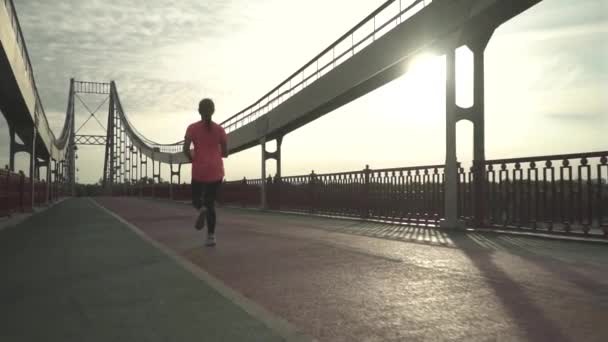 The girl is running on the bridge in the morning. The lady spends time outdoor alone. The woman leads a healthy lifestyle. Female moves in slow motion. - Imágenes, Vídeo
