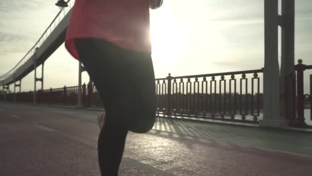 The girl is running on the bridge in the morning. The lady spends time outdoor alone. The woman leads a healthy lifestyle. Female moves in slow motion. - Footage, Video