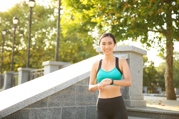 Sportieve Aziatische vrouw met fitness tracker buitenshuis - Foto, afbeelding