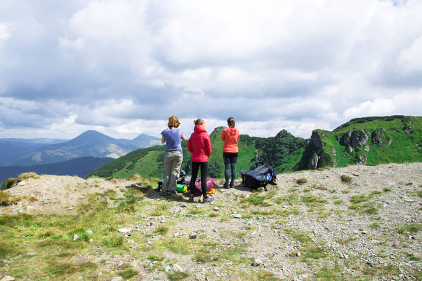 три неузнаваемые девушки на краю горы, смотрящие на зеленый альпийский пейзаж
 - Фото, изображение