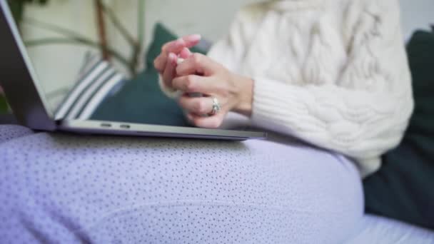 A woman freezes at home, wraps herself in a white knitted sweater and works on a laptop. Hygge concept. Close-up - Felvétel, videó