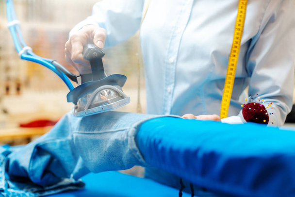Employee in textile cleaning ironing some trousers - Photo, Image
