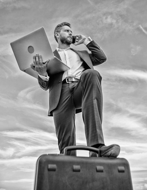 Man well groomed businessman holds laptop blue sky background. Guy formal suit modern technology manager entrepreneur put foot on briefcase. Top qualities excellent manager. Confident entrepreneur - Foto, afbeelding