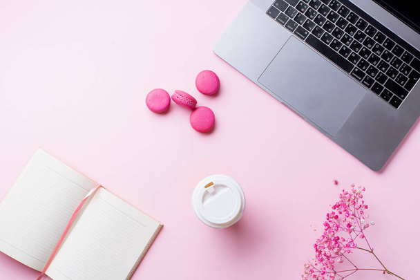 female blogger workplace with laptop and coffee to go cup with notepad and macaroons on pink background. Top view   - Φωτογραφία, εικόνα