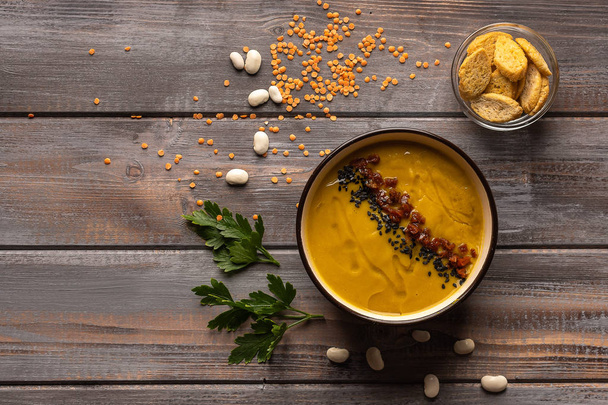 Cream soup with a mixture of beans and spices on a wooden background. near a vase with crackers. On the table beans and parsley leaves - Fotografie, Obrázek