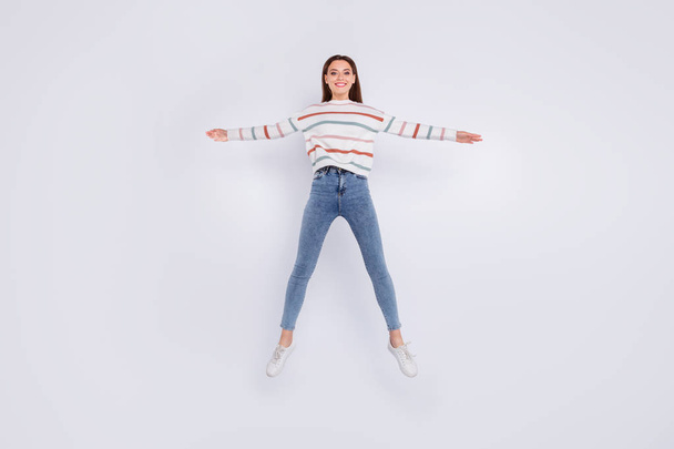 Full size photo of lovely person raising hands making star jumping wearing striped sweater denim jeans isolated over white background - 写真・画像