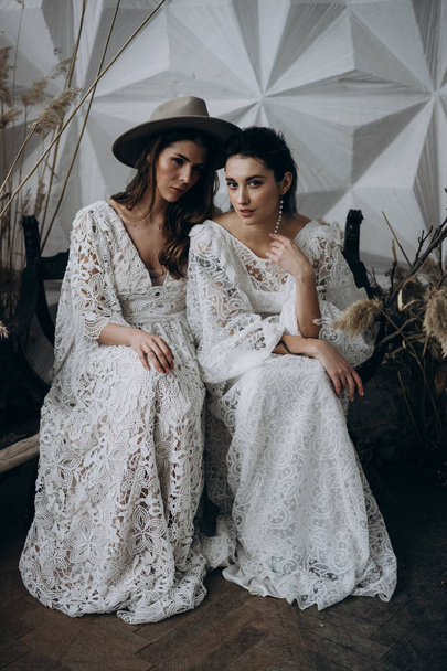 two models in white dresses sitting on wooden bench in the studio  - Valokuva, kuva