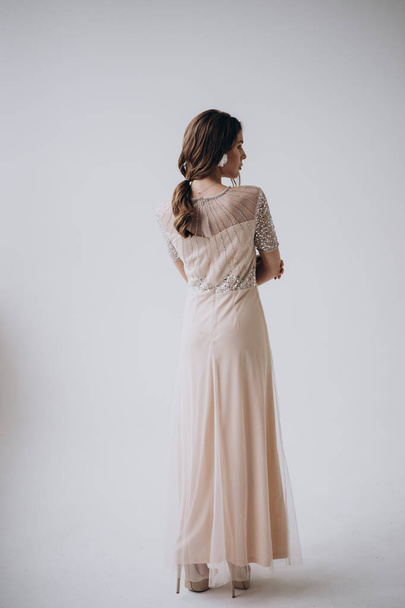 πίσω όψη της γυναίκας φορώντας μπεζ φόρεμα σε στυλ Μπόχο στέκεται στο φως φόντο  - Φωτογραφία, εικόνα
