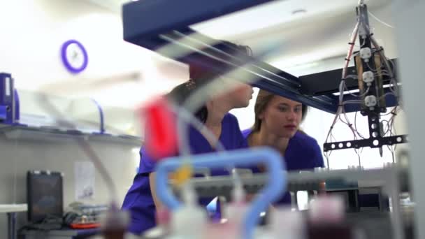 Dos mujeres jóvenes en uniforme azul y guantes de goma que controlan la fabricación de medicamentos en el laboratorio. Realización de investigaciones en el laboratorio. Ciencia, profesión, concepto de salud
 - Metraje, vídeo
