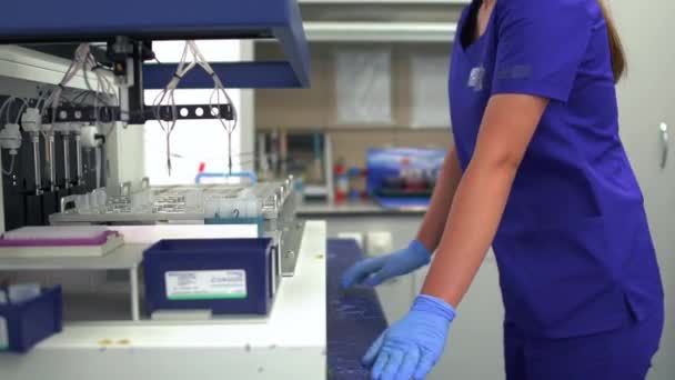 De jonge vrouw in blauw uniform en rubberen handschoenen controleren drugsproductie in het laboratorium. Onderzoek doen in een modern lab. Wetenschap, beroep, gezondheidszorg. Langzame beweging - Video