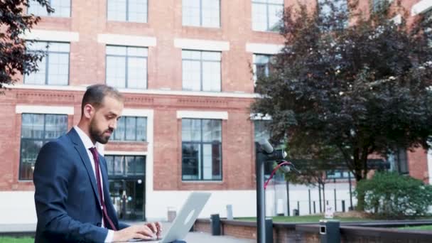 Empresario escribiendo al aire libre en el portátil sentado en un distrito de negocios
 - Metraje, vídeo