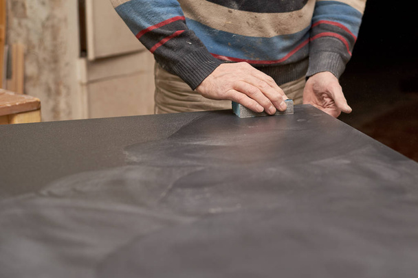 un hombre trata una superficie mate negro con una esponja con papel de lija
. - Foto, Imagen