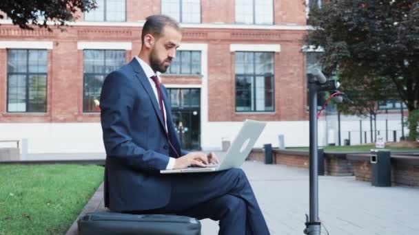 Mann im Anzug sitzt im Geschäftsviertel und arbeitet am Laptop - Filmmaterial, Video