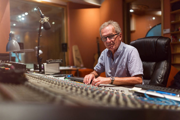 Чоловічий інженер середнього віку звукозапису в студії звукозапису, що сидить на багатоканальній консолі
 - Фото, зображення