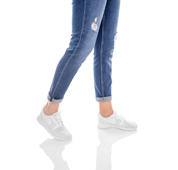 Benen in jeans en witte sneakers geïsoleerd op een witte achtergrond. - Foto, afbeelding