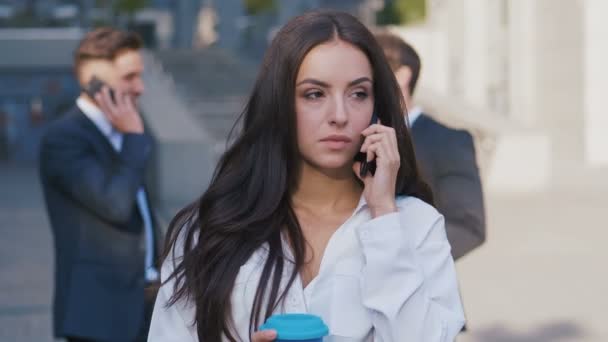 Beautiful Businesswoman talking on the Phone during Coffee Break on Streets of Business District near Office Building Business Center and group of Business People in the background. - Footage, Video