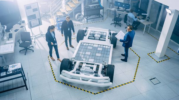 Team of Automobile Design Engineers in Automotive Innovation Facility. They are Working on Electric Car Platform Chassis Prototype that Includes Wheels, Suspension, Hybrid Engine and Battery. - Foto, Imagen