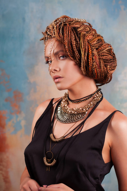 Southern flavor. Portrait of a luxurious tanned woman, pensive, stylish, with an exotic hairstyle and large jewels. - Fotografie, Obrázek