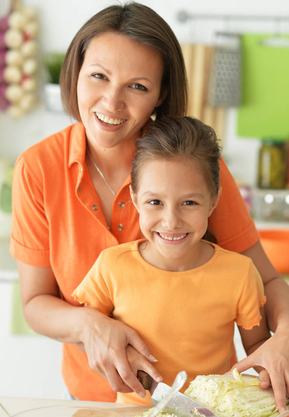 Cute little girl with her mother cooking together at kitchen table  - Foto, Imagen