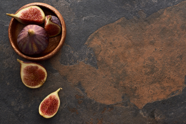 top view of ripe whole and cut delicious figs near wooden bowl on stone background - Fotó, kép