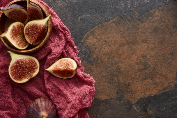 top view of ripe cut delicious figs in wooden bowl on rustic red cloth on stone background - Valokuva, kuva