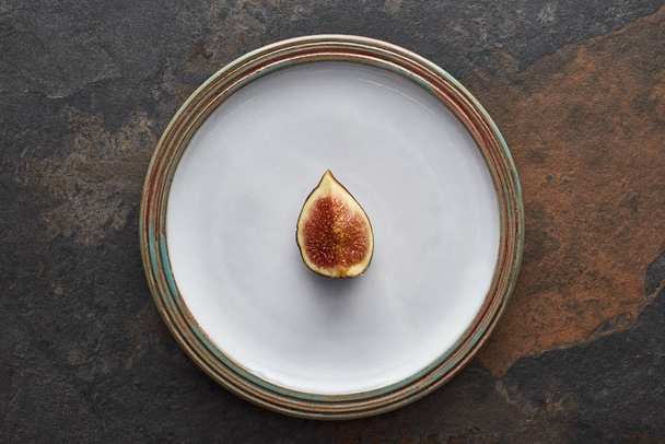 top view of ripe cut delicious fig on round white plate on stone background - Zdjęcie, obraz