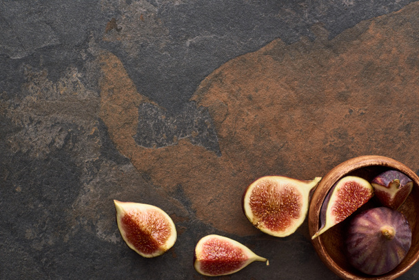 top view of ripe whole and cut delicious figs near wooden bowl on stone background - Foto, Imagem