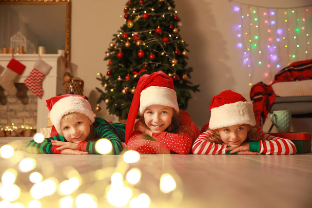 Schattige kleine kinderen in de Kerstman hoeden liggend op de vloer op kerstavond thuis - Foto, afbeelding