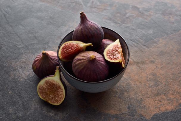 ripe whole and cut delicious figs in bowl on stone background - Fotó, kép