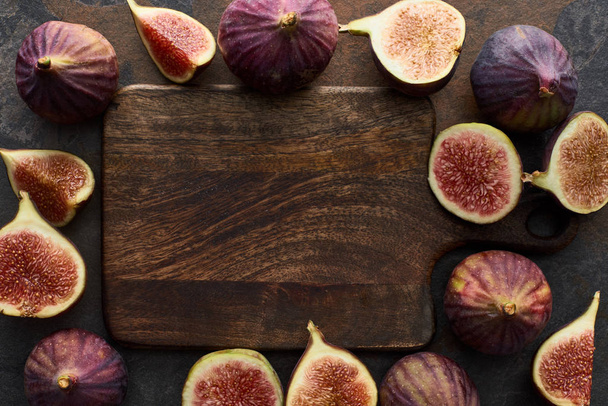 top view of ripe whole and cut delicious figs near empty cutting board on stone background - Fotó, kép