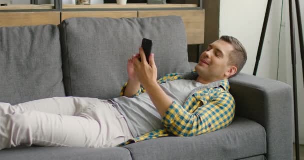 Young man has a video chat, lying on sofa at home - Felvétel, videó