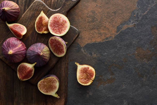 top view of ripe whole and cut delicious figs and wooden brown cutting boards on stone background - Фото, изображение