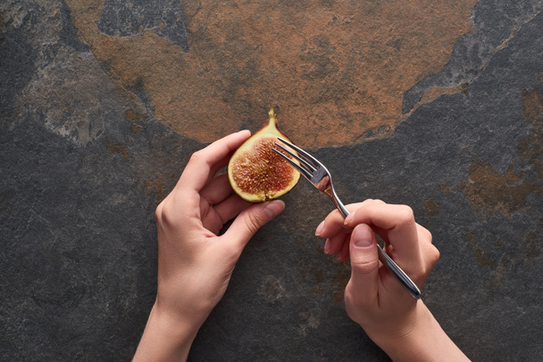 cropped view of woman holding fork and ripe delicious fig half on stone background - Photo, Image