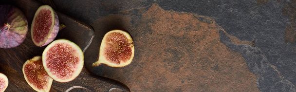 panoramic shot of ripe figs on brown wooden cutting board on stone background - Fotó, kép