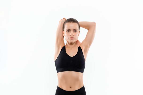 Joven mujer rubia deportiva en una ropa deportiva negro estiramiento antes de hacer ejercicio aislado sobre fondo blanco
. - Foto, imagen