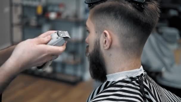 Vista de cerca en los hombres peinado en una peluquería con trimmer profesional. Corte de pelo para hombre en peluquería con cortador eléctrico. Aseo del cabello
. - Imágenes, Vídeo